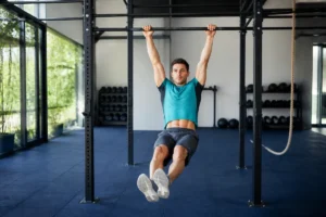 Athlète réalisant le kip du muscle up CrossFit sur une barre fixe dans une salle d’entraînement lumineuse