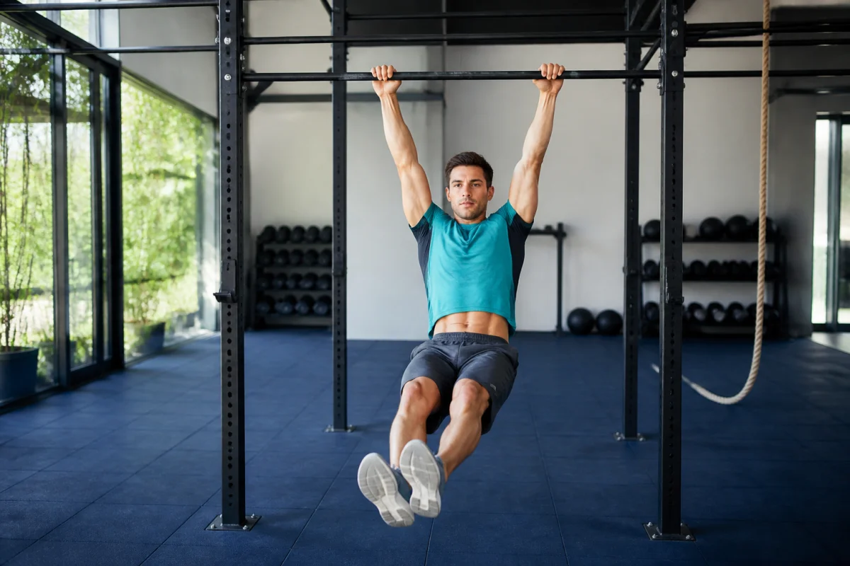 Athlète réalisant le kip du muscle up CrossFit sur une barre fixe dans une salle d’entraînement lumineuse